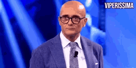 a bald man wearing glasses and a suit is standing on a stage with the words viperissima above him .