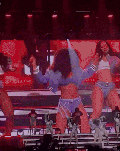 a group of women are dancing on a stage with a large screen behind them