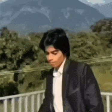 a man in a black jacket and white shirt is standing on a balcony .