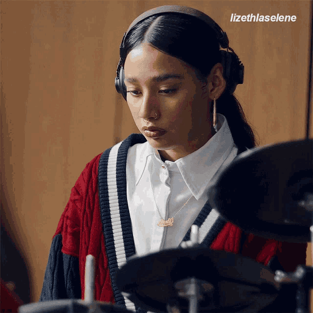 a woman wearing headphones and a necklace with the name lizeth is playing the drums