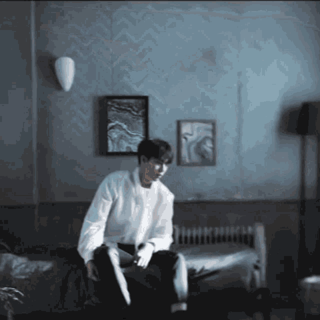 a man in a white shirt is sitting on a bed .