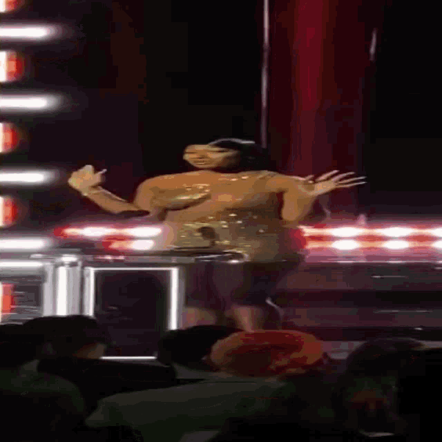 a woman in a gold dress is dancing on a stage in front of a crowd of people .