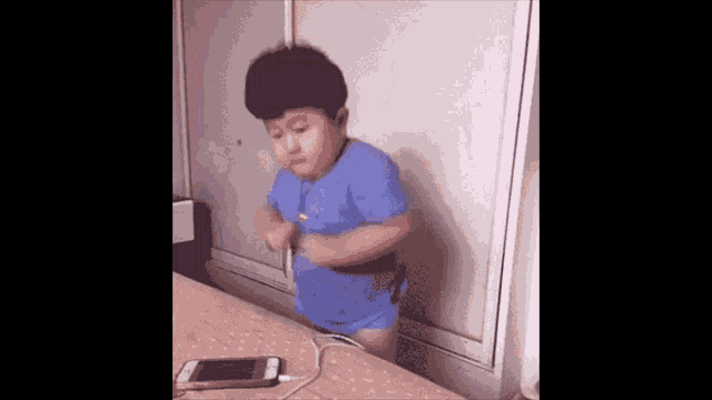 a young boy in a blue shirt is standing in front of a cell phone .
