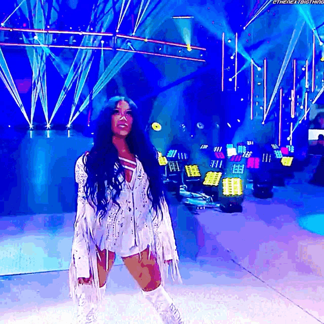 a woman in a white outfit is standing on a stage with a blue background