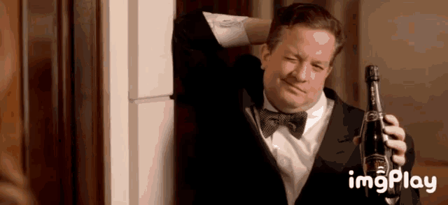 a man in a tuxedo and bow tie is holding a bottle of champagne ..