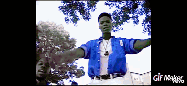 a man in a blue shirt is standing in front of trees with a gif maker logo below him