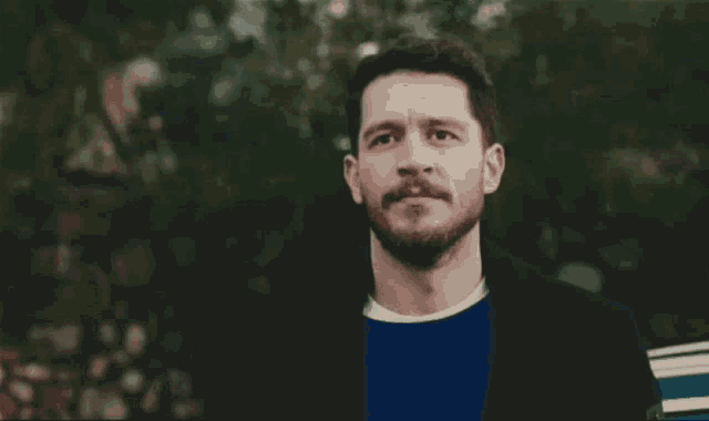 a man with a beard and mustache wearing a blue sweater and a black jacket .