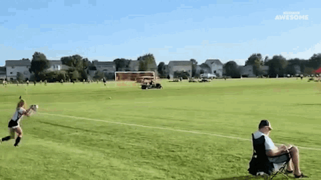 a man is sitting in a chair watching a girl throw a frisbee on a field
