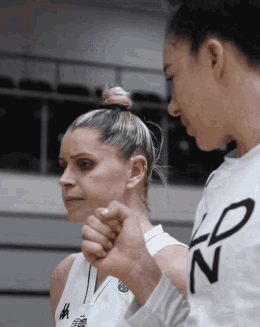 a woman wearing a ldn shirt holds another woman 's fist