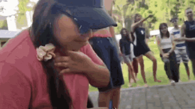 a woman wearing a hat and sunglasses is sitting on the ground with a group of people standing around her .