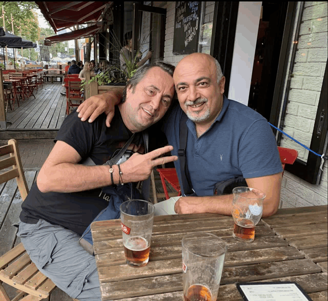 two men are sitting at a table with two glasses of beer and a menu on the table