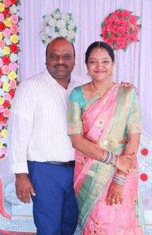 a man and woman pose for a picture in front of a wall of flowers