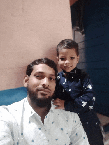 a man is holding a little boy in his arms and the photo was taken on an oppo a5 2020 phone