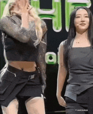 two women are standing next to each other on a stage and one is covering her face .