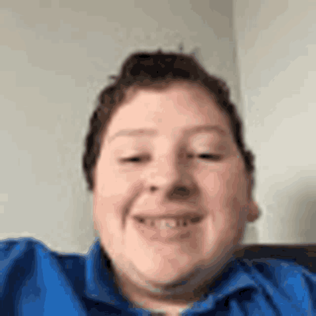 a young man in a blue shirt is smiling for the camera while sitting on a couch .