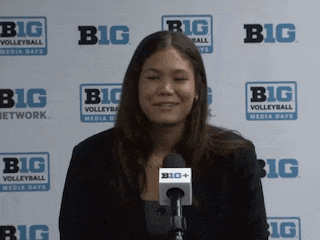 a woman is smiling in front of a big volleyball sign