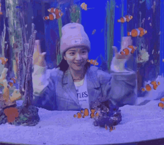 a woman in a pink hat is standing in front of an aquarium filled with fish .