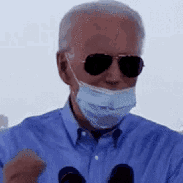 a man wearing a mask and sunglasses is giving a speech in front of two microphones .