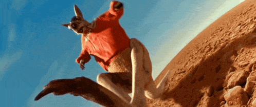 a kangaroo wearing a red shirt is jumping over a dirt hill