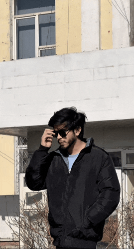 a man in a black jacket is standing in front of a building