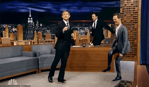 three men in suits are dancing in front of jimmy fallon .