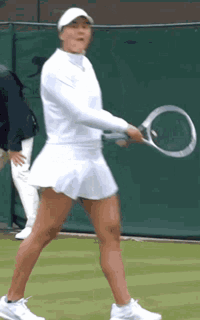 a woman in a white skirt is holding a tennis racket on a tennis court .
