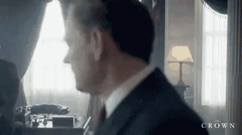 a man in a suit and tie is standing in a room in front of a window .