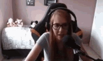 a woman wearing glasses and headphones is sitting in front of a microphone in a bedroom .
