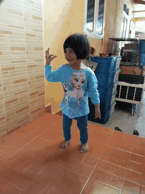 a little girl wearing a frozen shirt stands on a tile floor