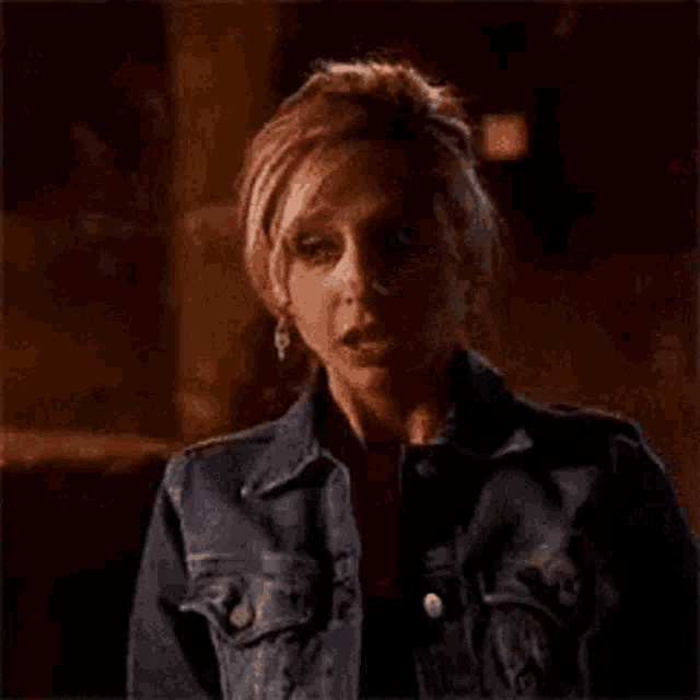 a woman is wearing a denim jacket and earrings and making a surprised face .