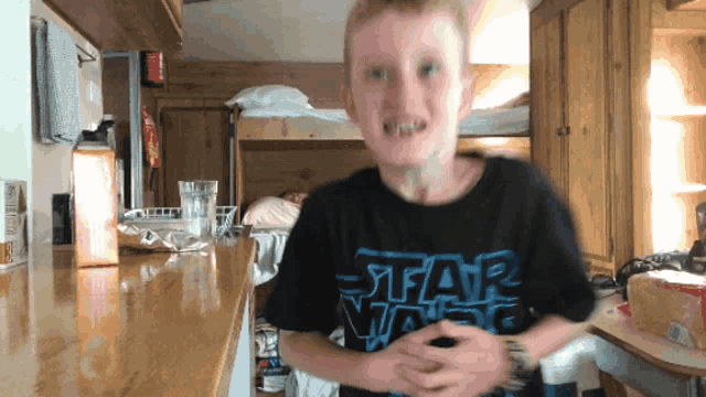 a boy wearing a star wars shirt is making a face