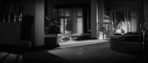 a black and white photo of a living room with a couch , chairs , and a window .