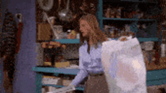 a woman in a blue shirt is carrying a large white bag in a room .