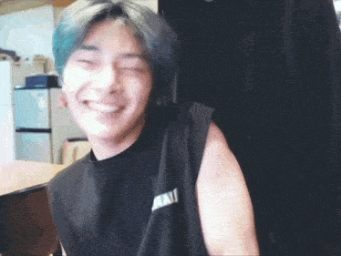 a young man with blue hair is smiling and wearing a black tank top with the letter a on it .