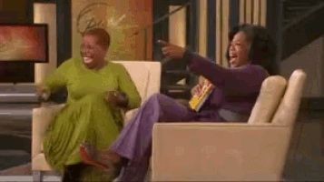 two women are sitting on a couch laughing together