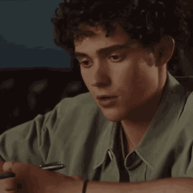 a young man with curly hair is writing in a notebook