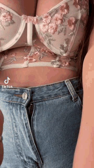 a woman wearing a floral bra and jeans has a tiktok sticker on her waist .