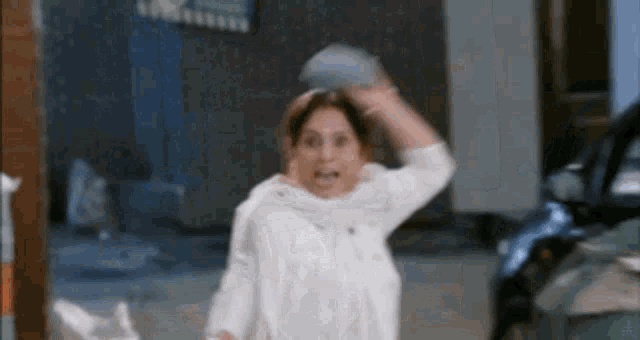 a woman in a white shirt is throwing a ball in the air while standing in front of a car .