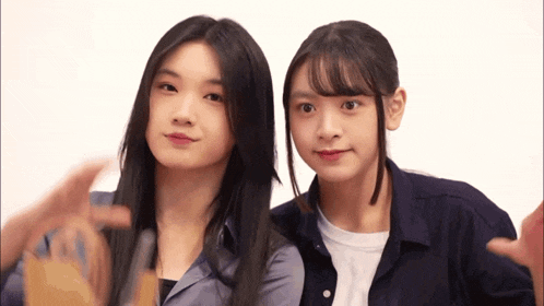 two girls are posing for a picture and one is making a heart with her hand