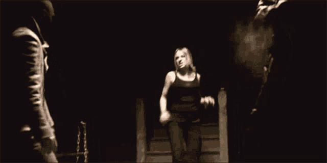 a woman in a black dress is kicking a chair in the dark