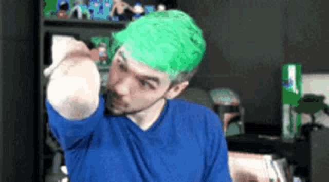 a man with green hair is wearing a blue shirt and giving a fist bump .