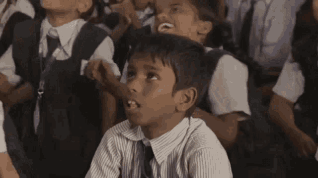 a boy in a striped shirt and tie is sitting in a classroom with other children