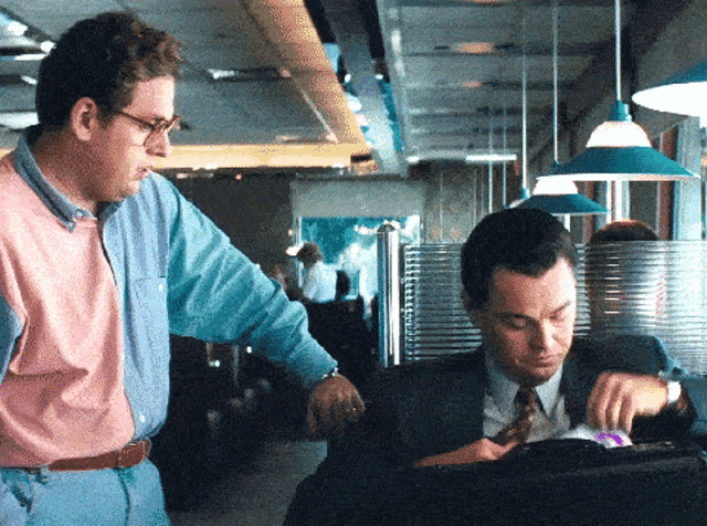 a man in a pink and blue shirt stands next to another man in a suit