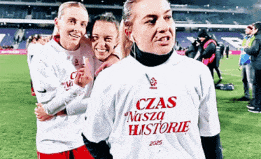 three women are posing for a picture on a soccer field with one wearing a shirt that says czas