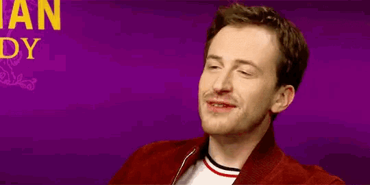 a man in a red jacket is laughing in front of a purple background with the word daddy in yellow letters