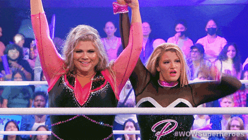 two female wrestlers are standing in a ring with their hands in the air