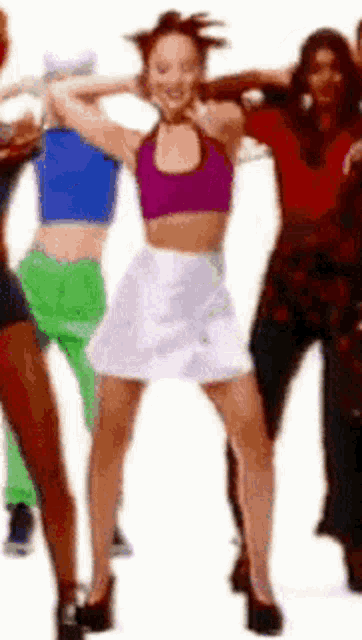 a woman in a purple top and white skirt is dancing with a group of women