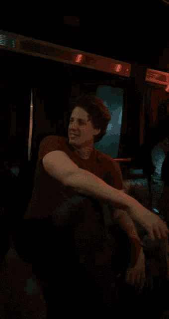 a man in a red shirt looks at the camera in a dark room