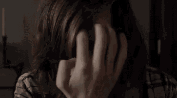 a woman is covering her face with her hands and looking at the camera .