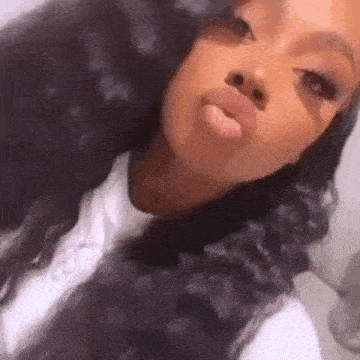 a woman with long black hair is taking a selfie and blowing a kiss at the camera .